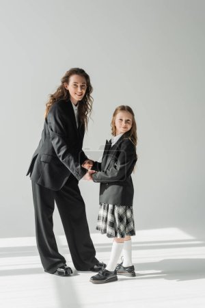 madre e hija, mujer feliz en traje de mano con colegiala en uniforme escolar con falda a cuadros, mujer de negocios, blazers, preparándose para el nuevo año escolar, mirando a la cámara
