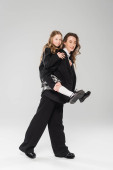mother piggybacking daughter in school uniform, working mom in business attire and schoolgirl on grey background in studio, modern parenting, fashionable family, having fun  Poster #659558016