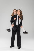 working mother piggybacking her happy daughter, businesswoman in formal attire and schoolgirl in uniform on grey background in studio, modern parenting, fashionable family, having fun  hoodie #659558042