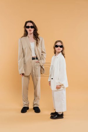 moderne Familie, Mutter und Tochter mit Sonnenbrille, stilvolle Geschäftsfrau und Mädchen in Anzügen posieren zusammen auf beigem Hintergrund, modische Outfits, formelle Kleidung, Corporate Mom 