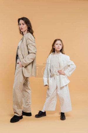 Photo for Stylish mother child concept, woman in suit and preteen daughter standing in suits on beige background, corporate mom, businesswoman, posing together, hand on hip, business style - Royalty Free Image