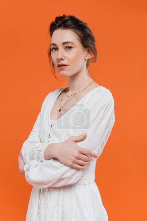 summer trends, model in sun dress looking at camera and standing with folded arms on orange background, stylish posing, lady in white, vibrant background, fashion, young woman 