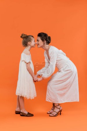 summer trends, young mother holding hands with happy preteen daughter and standing on orange background, white sun dresses, togetherness, fashion and style concept, bonding and love, nose to nose