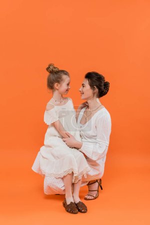 Sommertrends, fröhliche Mutter-Bindung mit Frühchen-Tochter auf orangefarbenem Hintergrund, weiße Sonnenkleider, Zweisamkeit, Mode- und Stilkonzept, Mutterliebe, Familienbindung 