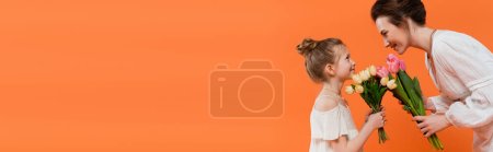 Photo for Happy mother and child with flowers, young woman and girl holding tulips and looking at each other on orange background, summer fashion, sun dresses, female bonding, banner - Royalty Free Image