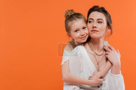 madre e hija, niña preadolescente alegre abrazando a la joven sobre fondo naranja, vestidos de sol blancos, crianza moderna, moda de verano, unión, amor