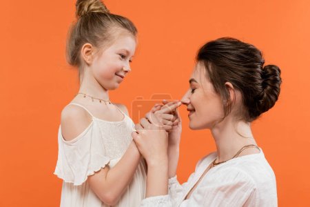 family moment, happy preteen girl touching nose of mother on orange background, white sun dresses, modern parenting, summer fashion, togetherness, love, female bonding 