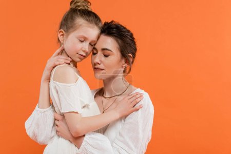 Mütterliche Liebe, Mutter und Tochter umarmen sich auf orangefarbenem Hintergrund, weiße Sonnenkleider, weibliche Bindung, moderne Elternschaft, Liebe und Fürsorge, Zweisamkeit 