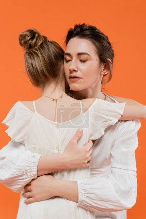 motherly love, caring mother hugging daughter on orange background, closed eyes, white sun dresses, female bonding, modern parenting, love and care, support, togetherness 