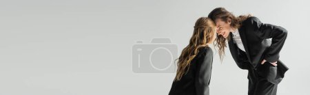 Photo for Mother and daughter having fun, happy woman in suit and schoolgirl in uniform looking at each other and smiling on grey background in studio, fashionable family, formal attire, banner - Royalty Free Image