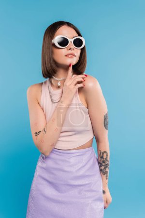 Modetrend, brünette junge Frau mit kurzen Haaren im Tank-Top, Rock und Sonnenbrille posieren auf blauem Hintergrund, Freizeitkleidung, Gen-Z-Mode, persönlicher Stil, Alltagsschminke, Freizeitkleidung 