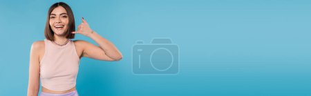 showing call me, happy young woman with short hair gesturing and looking at camera on blue background, casual attire, gen z fashion, personal style, nose piercing, positivity, banner 