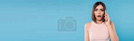Photo for Phone call, shocked young woman with short hair, tattoos and nose piercing talking on smartphone on blue background, casual attire, gen z fashion, opened mouth, emotional, banner - Royalty Free Image