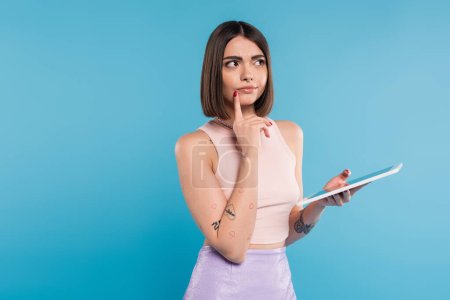brunette young woman with short hair, tattoos and nose piercing digital tablet laptop on blue background, generation z, summer trends, attractive, social media influencers, tablet user, pensive 
