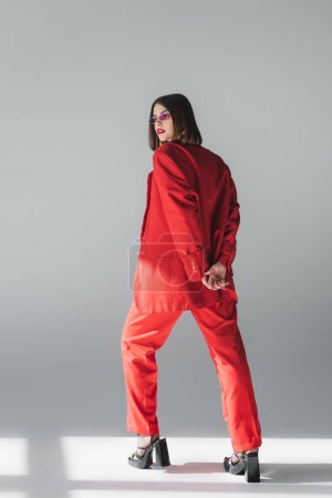 lady in red, young brunette woman with short hair posing in pink sunglasses and red suit on grey background, generation z, trendy outfit, fashionable model, professional attire, trendy outfit 