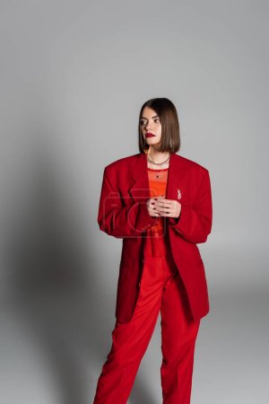Dame in Rot, junge brünette Frau mit kurzen Haaren und Nasenpiercing posiert im Anzug auf grauem Hintergrund, Generation Z, Führungsstil, modisches Modell, professionelle Kleidung, Führungsstil 