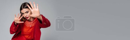 Foto de Vestimenta formal, joven morena con pelo corto posando en traje y extendiendo las manos sobre fondo gris, generación z, atuendo de moda, modelo de moda, atuendo profesional, pancarta - Imagen libre de derechos