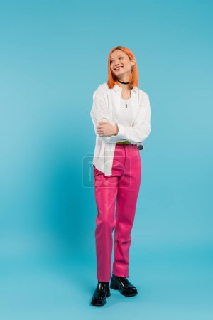 glückliches Gesicht, fröhliche asiatische junge Frau mit gefärbten Haaren, lässig gekleidet und lächelnd auf blauem Hintergrund, weißes Hemd, wegschauend, Halskette, rote Haare, Generation z, volle Länge
