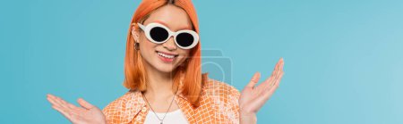 positive, jeune femme asiatique avec les cheveux teints debout en tenue décontractée et lunettes de soleil, geste avec les mains sur fond bleu vif, chemise orange, collier, génération z, cheveux rouges, bannière