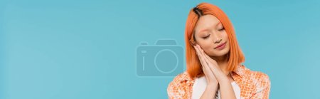 sleepy asian woman, young model with dyed red hair holding hands near face and posing with closed eyes on vibrant blue background, generation z, casual attire, tired, fatigue, exhausted, banner 