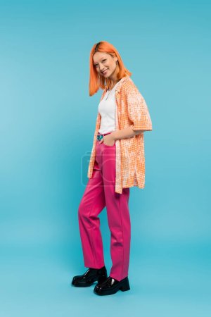 Photo for Radiant smile, full length, pretty and young asian woman with dyed hair  posing with hand in pocket on blue background, looking at camera, pink pants, generation z, modern style - Royalty Free Image