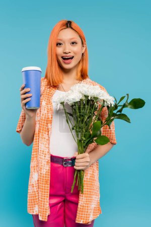 étonné, visage heureux, asiatique et jeune femme aux cheveux roux tenant du café à emporter et bouquet de fleurs sur fond bleu, tenue décontractée, génération z, culture du café, boisson chaude, tasse en papier