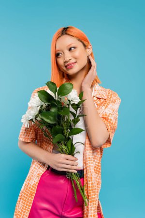 sensualidad, mujer asiática alegre con pelo rojo sosteniendo flores blancas sobre fondo azul, atuendo casual, generación z, ramo floral, vibraciones de primavera, cara feliz, generación z, cultura juvenil 