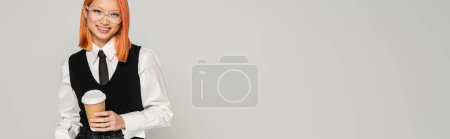 fröhliche Emotion, junge und glückliche Asiatin mit Coffee to go vor der Kamera auf grauem Hintergrund, jugendliche Mode, Business Casual, schwarz-weiße Kleidung, stylische Brille, Banner