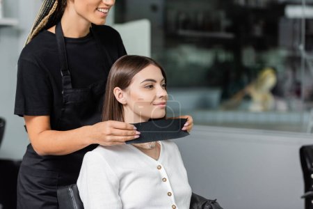 Salon-Job, glückliche Beauty-Arbeiterin trägt Friseurkragen auf weibliche Klientin in Schönheitssalon, Friseur, Frisur, Verlängerung, Haarbehandlung, Salon-Kunde, Beauty-Beruf, tätowiert