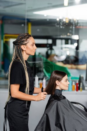 Photo for Beauty industry, hair stylist with braids wearing hairdressing cape on female client, hair extension, hair treatment, salon customer, beauty profession, salon work, hair make over, side view - Royalty Free Image