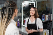 salon services, positivity, tattooed beauty worker in apron welcoming female client with braids in salon, beauty industry, salon job, customer in salon, hairdresser, hair professional  puzzle #660917232