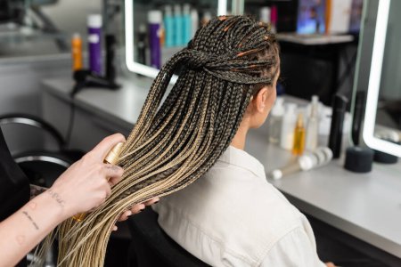 Photo for Hair salon, tattooed hairdresser applying hair product on braids of woman in salon, spray bottle, happy beauty worker, client satisfaction, salon customer, beauty worker, back view, crop - Royalty Free Image