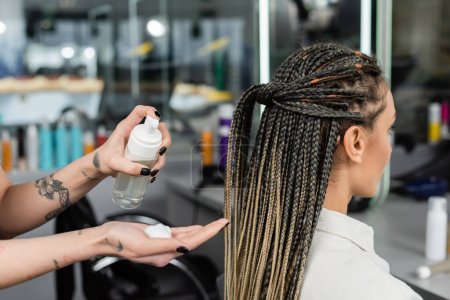 client satisfaction, hair product, tattooed hairdresser with styling foam in hand, woman with braids in salon, bottle, beauty worker, salon customer, beauty worker, hair professional 