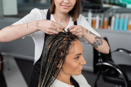 beauty industry, braids, tattooed hairdresser braiding hair of woman in salon, braiding process, salon customer, beauty profession, client satisfaction, hair fashion, hairdo 