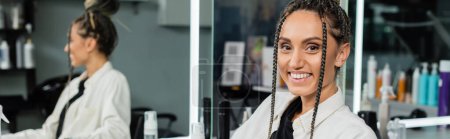 Photo for Happy client in beauty salon, cheerful woman with hair bun looking at camera, customer satisfaction, hair salon, hairstyle, female client with braids, looking at camera, mirror refection, banner - Royalty Free Image