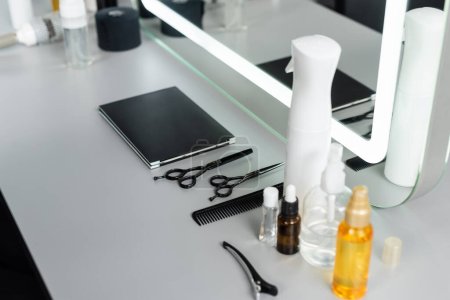 outils de salon professionnel, ciseaux de coiffure, bouteilles, huile capillaire, pince à cheveux, peigne, livre de palette de cheveux près du miroir dans le salon de beauté, essentiels de cheveux, industrie de la beauté, mode de cheveux 