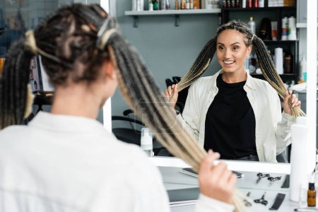 happy client in beauty salon, cheerful woman with braids looking at mirror, customer satisfaction, beauty salon, hairstyle, female client with braids,  mirror refection, two ponytails, extension 