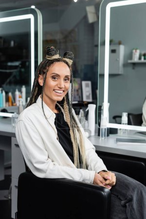 happy woman in beauty salon, joyful client with braids looking at camera, customer satisfaction, hair salon, hairstyle, female client with hair buns,  mirror refection, braided hair 
