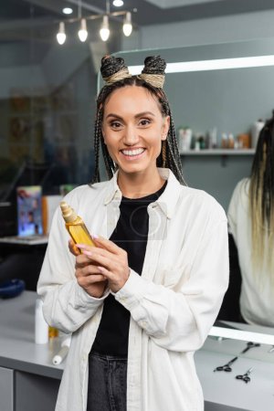 happy woman in beauty salon, joyful client with braids looking at camera, customer satisfaction, hairstyle, female client with braids, holding hair oil, hair buns, braided hair, portrait 