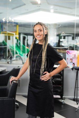 happy hairdresser, woman with braids in beauty salon, hair extension, beauty worker, salon work, hair trends, positivity, interior, profession, salon industry, professional headshots 