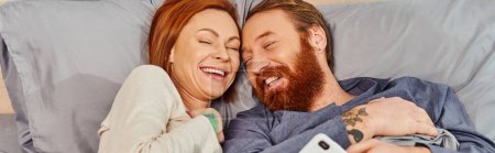 carefree redhead couple spending quality time without kids, day off, cheerful husband and wife, bearded man, smiling woman, comfortable living, cozy bedroom, laughing, banner 
