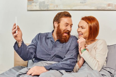 excited bearded man with smartphone, digital couple, screen time, networking, relaxing on weekends without kids, husband and wife, tattooed, day off, enjoying time 