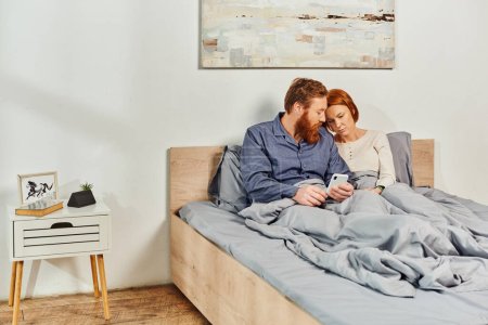Photo for Digital couple, screen time, networking, relaxing on weekends without kids, sad husband and wife, bearded man and redhead woman using smartphone, childfree, day off, tattooed couple, interior - Royalty Free Image