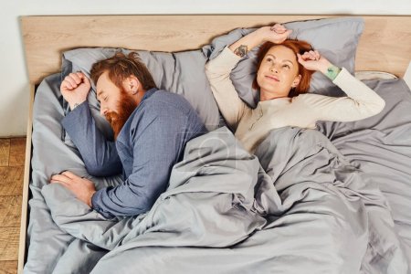 quiet house, parents alone at home, redhead husband and wife in cozy bedroom, bearded man sleeping near carefree woman relaxing on weekends, day off, wake up, tattooed, enjoy, top view 
