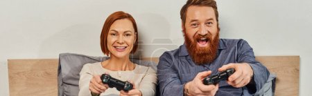 weekends without kids, redhead husband and wife playing video game, bearded man and happy woman holding joysticks, excited, gaming fun, married couple, modern lifestyle, banner 