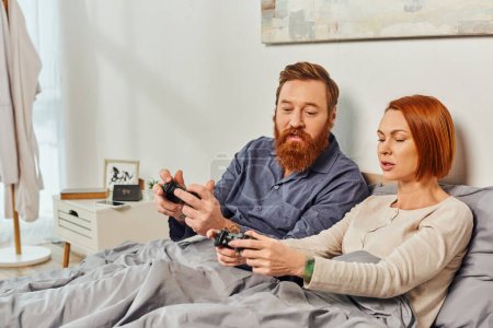 day off without kids, redhead husband and wife playing video game, bearded man and tattooed woman holding joysticks, gaming fun, married couple, modern lifestyle, joy of gaming 