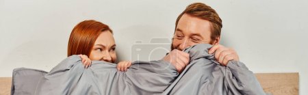 day off without kids, redhead husband and wife looking at each other, hiding behind blanket, married couple, modern lifestyle, happiness at home, relaxation time, parents alone at home, banner 