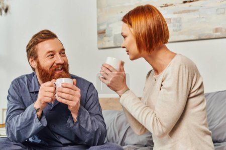 Photo for Morning rituals, quality time, day off without kids, redhead husband and wife, bearded man and woman holding cups, coffee and conversation, happy parents alone at home, lifestyle, adult leisure - Royalty Free Image