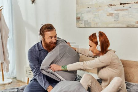 Photo for Parents alone, having fun, shared music, redhead husband and wife, happy couple in wireless headphones pillow fight, bearded man and carefree woman, tattooed people, day off without kids - Royalty Free Image