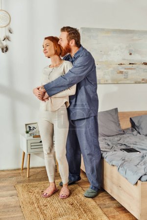 full length of married couple hugging in cozy bedroom, day off without kids, redhead husband and wife, enjoying time together, weekends together, tattooed, parents alone at home  magic mug #661667728